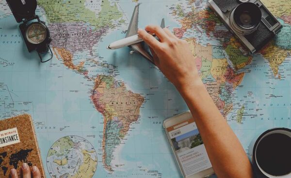 11Photo d'une carte du monde avec une main tenant un avion au dessus de l'Atlantique. Illustration pour l'article Voyage et Maison de retraite sont-ils compatibles ?
